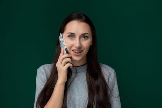 A woman standing outdoors, engaged in a phone conversation on her cell phone. She holds the device to her ear, speaking animatedly while surrounded by urban surroundings.
