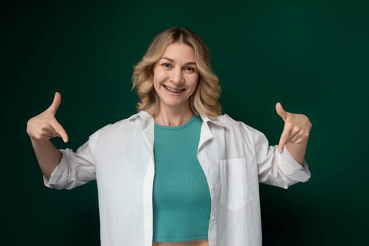 A woman wearing a green top and white jacket stands outdoors. She looks confident and stylish, exuding a sense of sophistication in her attire. The contrast between the green and white colors enhances her overall appearance.