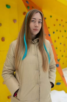 A woman with long hair is standing in front of a climbing wall, ready to engage in a challenging climb to reach the top. She is wearing climbing gear and appears focused on the task ahead.