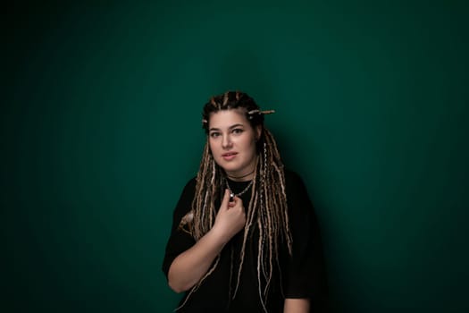 A woman with dreadlocks is standing in front of a vibrant green wall. She is looking directly at the camera with a confident expression. The contrast between her hair and the wall creates a striking visual impact.