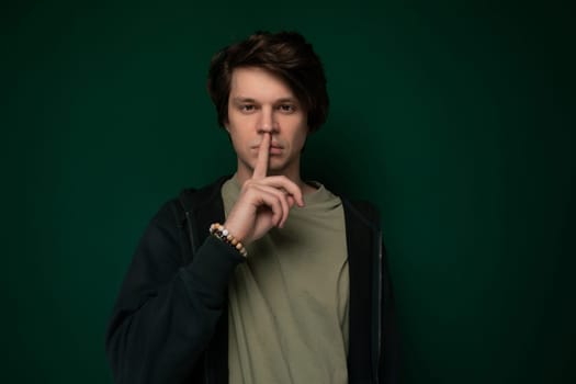 A man is shown with his index finger pressed against his lips in a hushing gesture. He appears to be signaling for silence or secrecy in a specific situation.