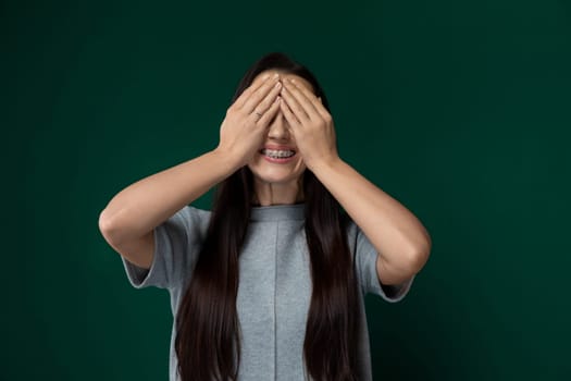 A woman is covering her eyes with her hands, blocking out external visual stimuli. She appears to be shielding her eyes from something or possibly expressing distress. Her hands are pressed firmly against her face, creating a barrier between her eyes and the surrounding environment.