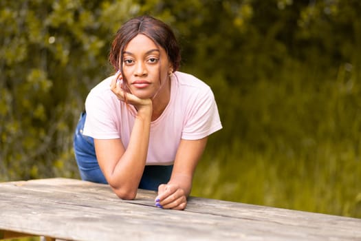 Young, beautiful black woman leaning on a bench in a park on an autumn afternoon.