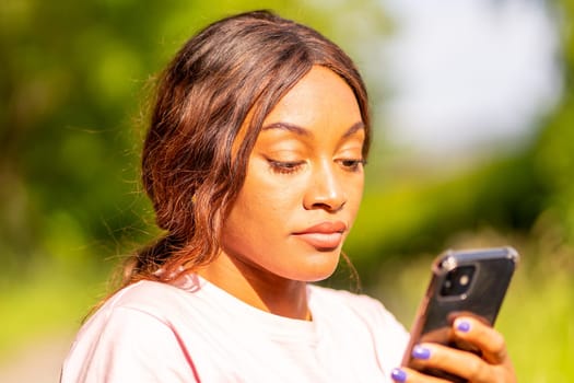 Young black woman with her phone chatting with her friends in a park on an October afternoon.