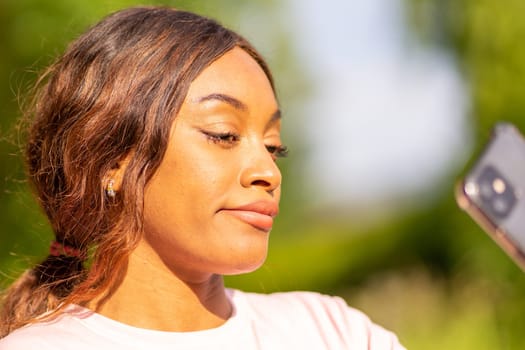 Young black woman with her phone taking selfie in a park on an October afternoon.