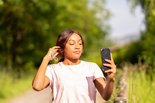 Young black woman with her phone taking selfie in a park on an October afternoon.