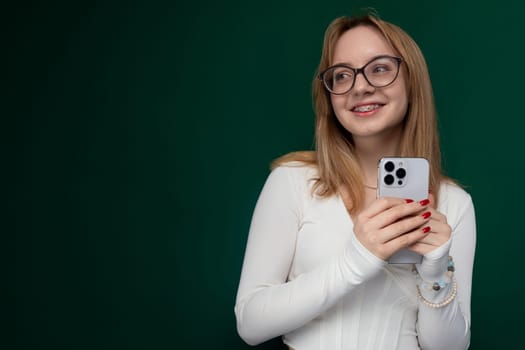 A woman wearing glasses is holding a cell phone in her hands. She appears to be focusing on the devices screen, possibly texting or browsing. The background is blurred, emphasizing her action.