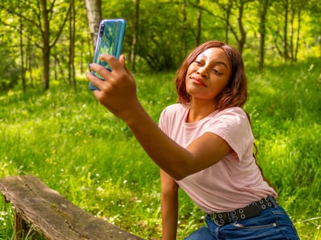 Young black woman with her phone taking selfie in a park on an October afternoon.