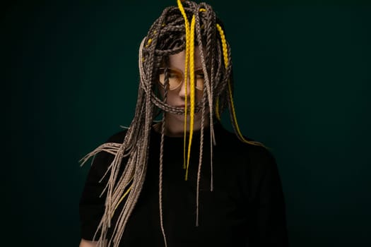 A woman with dreadlocks is standing in front of a solid green background. She has a confident posture and is looking directly at the camera.