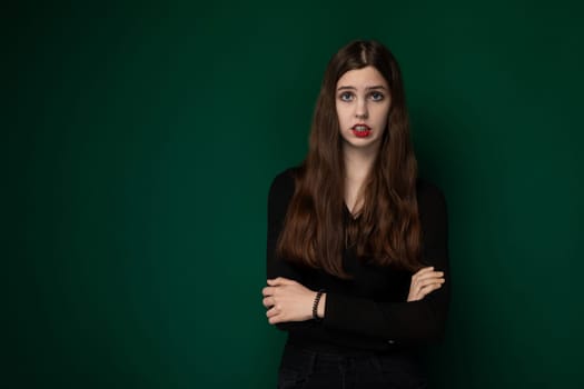 A woman stands with her arms crossed in front of a vibrant green background. She appears confident and determined, showcasing a sense of strength and poise.