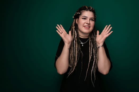 A woman with dreadlocks is standing against a solid green background. She appears confident and is looking directly at the camera.
