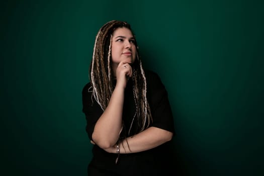 A woman with dreadlocks stands confidently in front of a vibrant green wall. Her hair cascades down her back, creating a striking contrast against the walls color.
