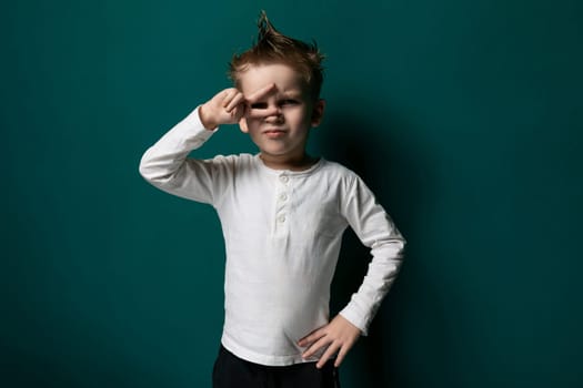 A young boy is standing in front of a vibrant green wall, looking straight ahead. He appears curious and engaged, possibly at a playground or school. The wall provides a bright background for the image.