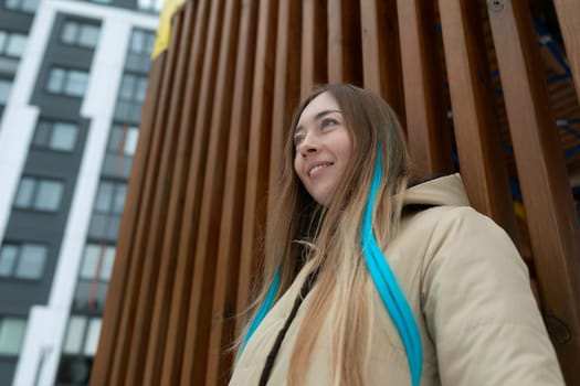 A woman with long hair is standing confidently in front of a tall building. She appears poised and elegant, gazing ahead. The buildings architecture is modern and sleek, contrasting with her flowing hair.
