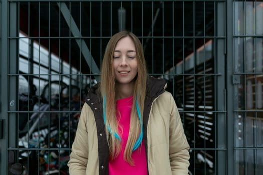 A woman stands in front of a metal gate, looking ahead. She appears contemplative or determined, her posture alert. The gate is tall, with intricate ironwork, and bars her path.