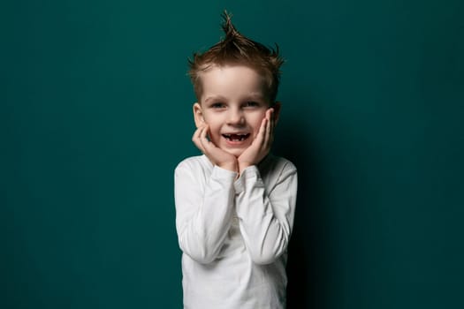 A young boy is standing upright in front of a vibrant green wall. He appears to be looking directly at the viewer, with a curious and innocent expression on his face. The boy is wearing casual clothing and does not seem to be interacting with anyone or anything else in the scene.