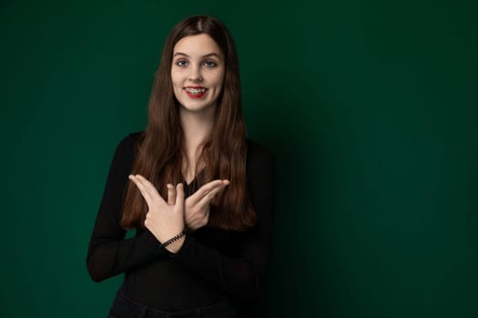 A woman is standing in front of a painted green wall, her posture upright and her expression neutral. The wall serves as a simple backdrop to the womans presence, creating a stark contrast between her figure and the vibrant color behind her.
