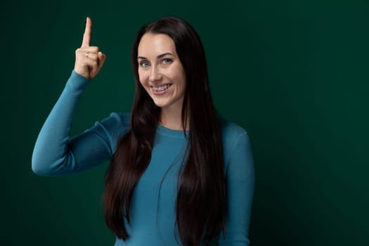 A woman with long black hair is standing and pointing to the side. She appears focused and engaged as she gestures towards something off-camera. Her hair cascades down her back, adding to the visual appeal of the scene.