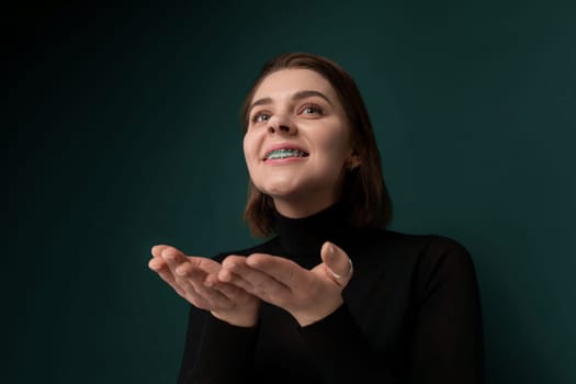 A woman is standing in front of a vibrant green wall, looking straight ahead. She appears to be posing or waiting, with a calm expression on her face.