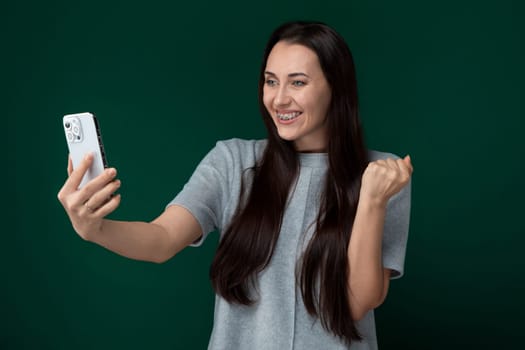 A woman holding a cell phone, posing for a selfie. She is smiling and looking at the phones screen while taking the picture.
