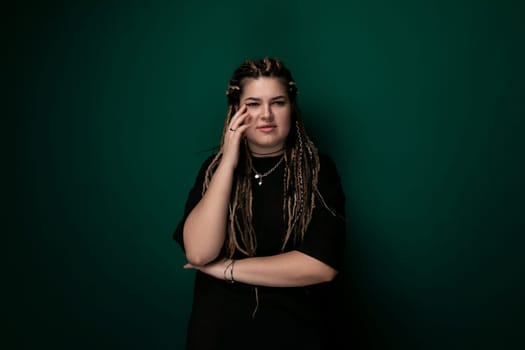 A woman with dreadlocks is seen standing against a vibrant green wall. She appears confident and stylish as she poses for the camera.