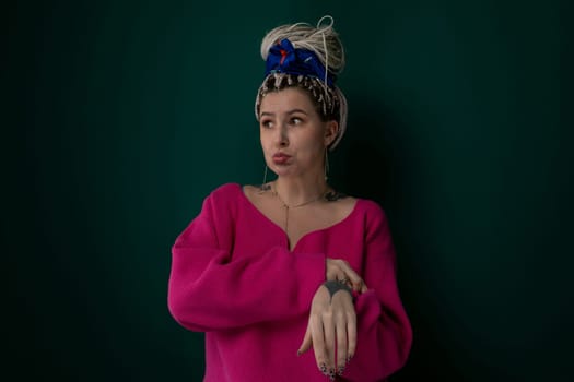 A woman is dressed in a pink sweater and a blue hat. She is standing or sitting, showcasing her outfit against a plain background.