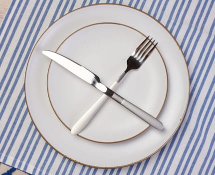 Round empty white ceramic plate, knife and fork crossed, top view