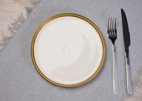 Round empty white ceramic plate, knife and fork on the table, top view