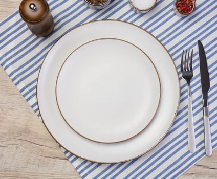 Round empty white ceramic plate, knife and fork on the table, top view