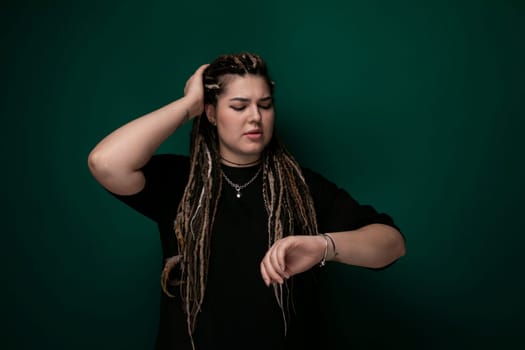 A woman with dreadlocks standing confidently in front of a vibrant green wall. She appears stylish and fashionable, showcasing her unique hairstyle against the bold background.
