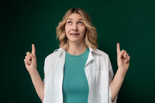 A woman wearing a green shirt is raising both of her hands up in the air in a standing position.