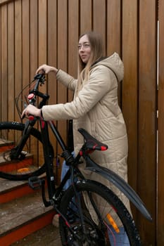 A woman is standing next to her bike on a set of steps. She appears to be taking a break or adjusting something on her bicycle. The surroundings are urban, with buildings in the background.