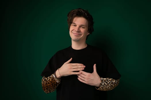 A man is standing in front of a vibrant green wall. He appears to be looking directly at the camera with a neutral expression. The background is simple and focuses solely on the man and the wall.