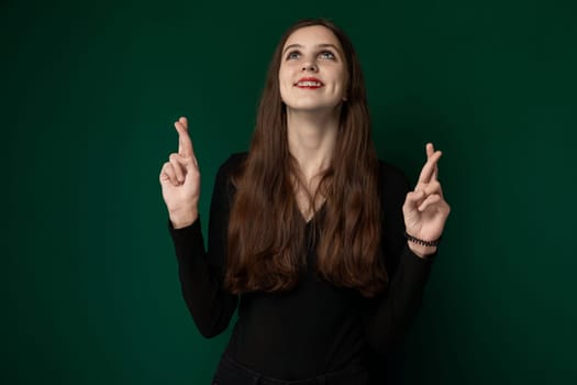 A woman stands upright in front of a solid green wall, looking directly at the viewer. She appears confident and poised, with a neutral expression. The background is a uniform shade of green, providing a simple yet striking backdrop to the subject.