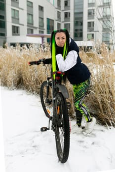 A woman is seen riding a bike in the snow-covered landscape, with the snowflakes falling around her. She is dressed warmly and seems to be enjoying the winter ride.