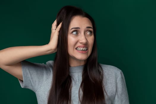 A woman with braces holding her hair in front of her face, showcasing her dental treatment. The womans face is partially obscured by her hair, emphasizing her braces as the focal point of the image.