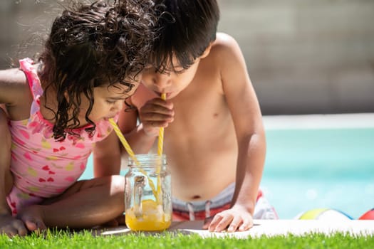 Two kids enjoy drinking a cold orange juice in a summer holidays pool.Summer holidays and family concept.