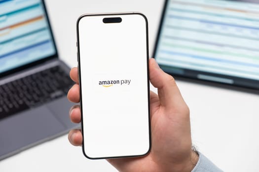 PRAGUE, CZECH REPUBLIC - JANUARY 21 2024: Amazon pay logo on the screen of smartphone in mans hand on the workplace background.