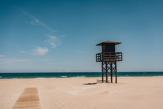 A solitary lifeguard tower standing on an empty, sandy beach with the sea and sky in the background. Sant Antoni beach, Cullera, Spain