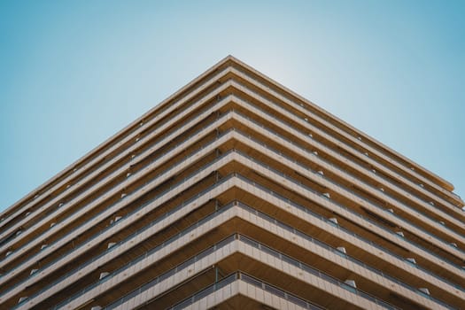 Unique perspective of a building s corner facade with balconies, set against a clear sky. Sant Antoni beach, Cullera, Spain