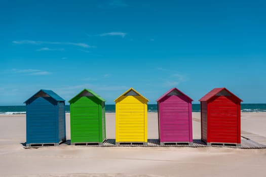 Brightly colored beach huts aligned on the sandy shore with the ocean in the background. Sant Antoni beach, Cullera, Spain