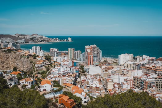 A panoramic view of a coastal cityscape with various buildings and the ocean in the background. Sant Antoni beach, Cullera, Spain