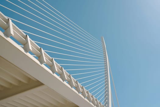 Close-up of modern bridge cables set against a clear blue sky. The image captures the precise lines and engineering details, emphasizing the minimalist and structural beauty of the bridge.