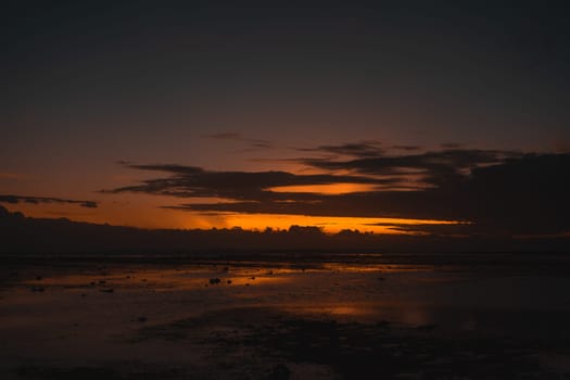 A scenic beach sunset with dramatic clouds and reflections in the wet sand. The vibrant colors create a stunning, serene scene, showcasing the natural beauty of the coastal landscape.