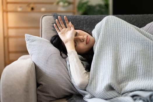 Young woman with the flu resting on a sofa, covered in a blanket, demonstrating the concept of feeling sick and healthcare