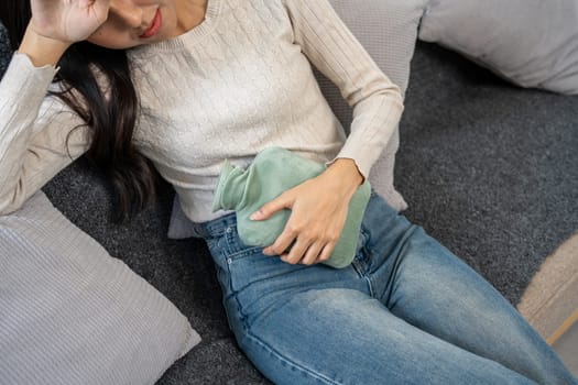 Young woman lying on a sofa, using a heat pad to relieve menstrual pain, demonstrating the concept of menstrual pain management