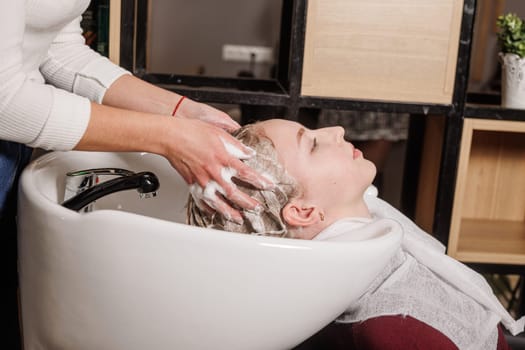 beauty salon master washes client's hair with shampoo for hair care in beauty salon, professional hairdresser,