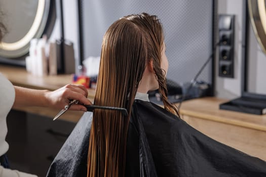 beauty master combing client's wet hair in beauty salon close-up, self-care concept, professional hair care