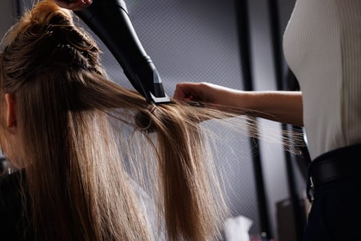 hairdresser drying hair with hair dryer and comb in beauty salon, drying hair close up, self care concept