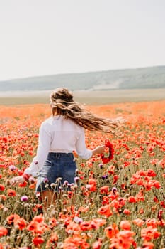 Happy woman in a poppy field in a white shirt and denim skirt with a wreath of poppies on her head posing and enjoying the poppy field